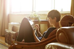 Young woman curled up on chair uses digital tablet