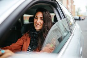 Young woman driving a sedan with a smile on her face.