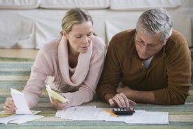 Couple preparing tax returns at home with calculator and paperwork on living room floor