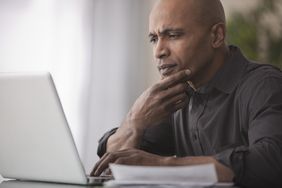 A person staring intently at the screen of a laptop with a hand on its keyboard