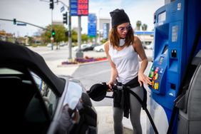 Woman with hat and glasses fills car with gas at the station