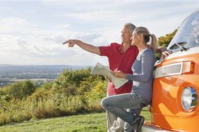 Retired couple looking at a map beside a camper van parked on a hillside