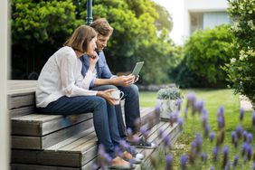 Man and a woman sit on steps looking at a tablet