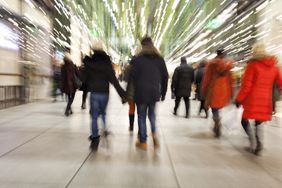 Large group of motion blurred people in winter coats walking in hallway with bright lights