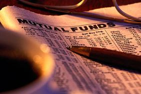 Finance section of newspaper folded to mutual funds listings placed under a pen, glasses and a cup of coffee