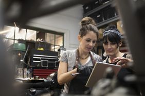 Women motorcycle mechanics with digital tablet working in auto repair shop