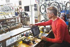 business owner of bike shop working behind counter on laptop