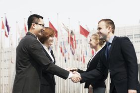 Two Asian people shaking hands with two Caucasian people in front of many flags in Beijing