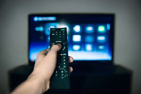 Close-up of male hand using remote control with television in background