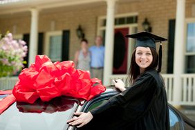 Graduate standing next to car with huge bow on it.