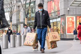 A person wears a face mask while carrying shopping bags.