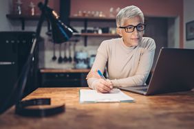 Bespectacled woman taking notes while working on laptop