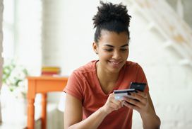 Smiling teen using credit card on phone at home