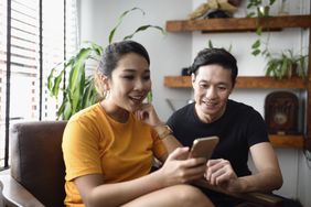 Smiling couple reading from a smartphone together at home