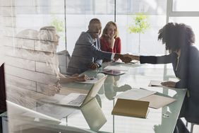 Businessman and businesswoman handshaking across conference table in meeting