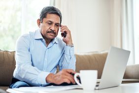 person in blue button-down shirt speaking on the phone in front of laptop