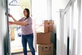 A woman enters a new house with boxes.