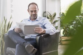  person in suit sitting in chair reading paperwork on his tablet