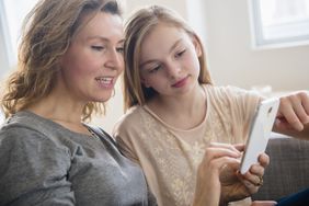 Caucasian mother and daughter using cell phone in living room