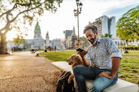 Mature man with beard and stylish casual clothing in springtime day in Buenos Aires, Argentina walking his dog
