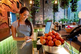 Woman Working at a Restaurant Weighing Tomatoes in a Bowl Smiling