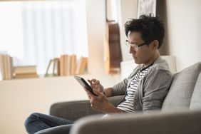 A man reads a tablet on a couch.