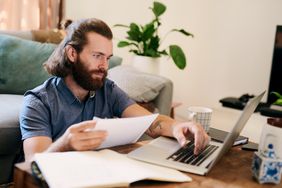 young man working remotely at home with paperwork in hands