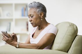 Woman looks at cell phone while sitting in a chair at home