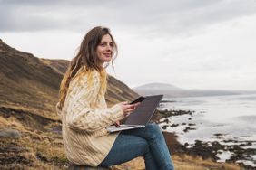 Iceland, woman using laptop and cell phone at the coast