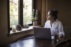 Woman working on laptop computer at home stares out of window pensively