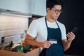 A man in an apron holds a credit card and a phone.