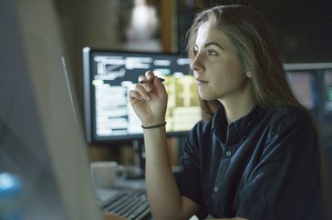 Young woman is seated at a desk surrounded by monitors displaying data