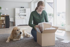 Woman opening a package with her dog watching