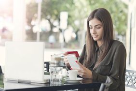 A woman at a cafe table considers how she should pay for her latte: credit account or credit card?