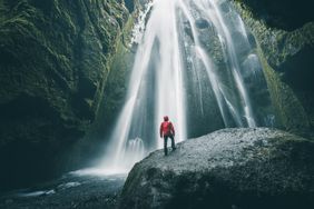 Tourist on a rock admiring Gljufrabui waterfall, Iceland