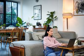 Woman sits on floor at coffee table with a laptop