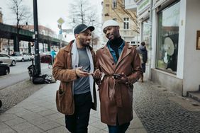 Two men talk while walking down the street.