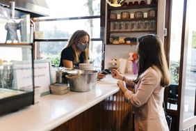 Young businesswoman paying through credit card at counter in coffee shop during COVID-19 - stock photo