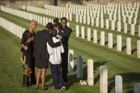 Multigenerational family dressed in black hugs at military cemetery