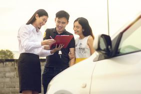 Happy Asian Couple purchasing and signing sales contract for car at dealership