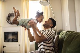 Father throws toddler daughter in the air in living room