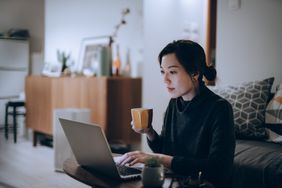 Woman working at home on a laptop while holding a mug