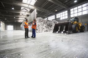Workers in paper recycling hall with waste paper