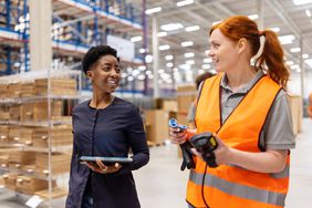 Businesswoman walking with a warehouse employee in orange vest