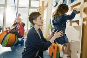 Preschool teacher helping little girl climb wall