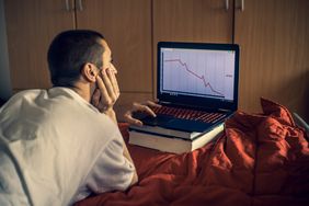 Man watching stock market crash on laptop screen in bedroom