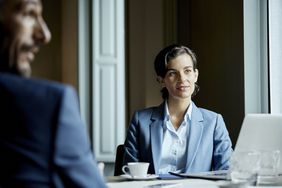 A woman in business attire listens in a meeting at a conference table.