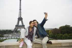 Couple sitting on wall, man taking photo, Eiffel tower in background