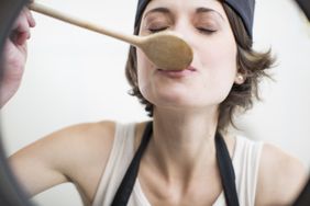 Female chef tasting food from saucepan in commercial kitchen