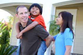 Smiling couple with a child standing outside a home